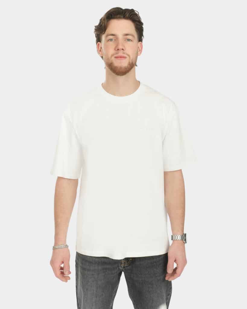Male model wearing the Own The Sky Tee in White, front view, with a subtle tonal Last Bucks chest logo and a relaxed fit