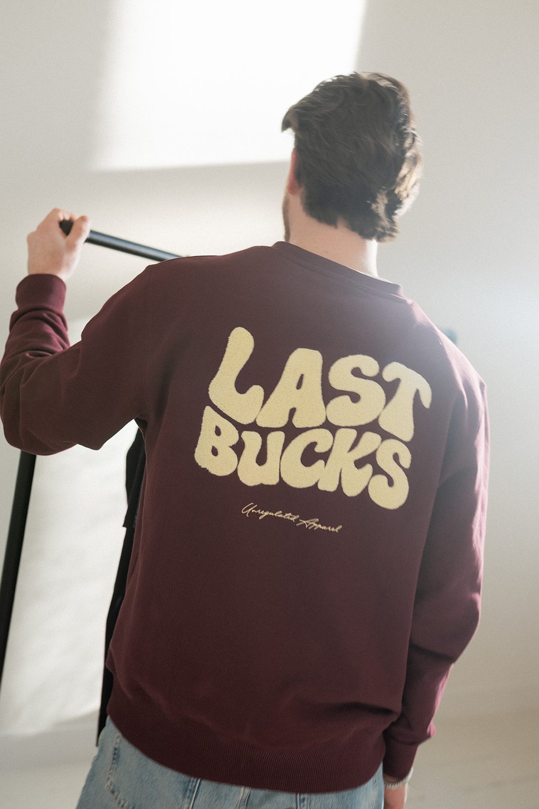 Rug van een bordeaux sweater met grote Last Bucks-print, de plek waar wij de naam zetten