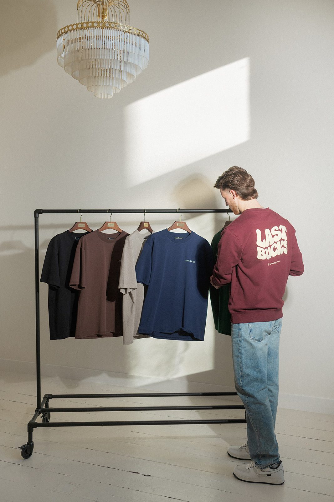 Man in bordeaux sweater naast een kledingrek met vijf tees, wat wij hebben in plaats van wat Miu Miu niet heeft