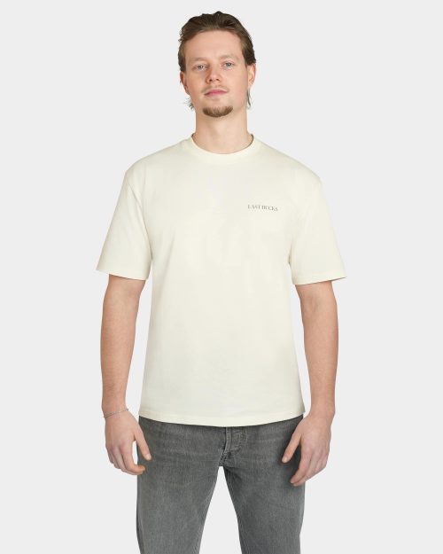 Model wearing the Uncaged Birds Tee in Off-White, front view with subtle “LAST BUCKS” chest print