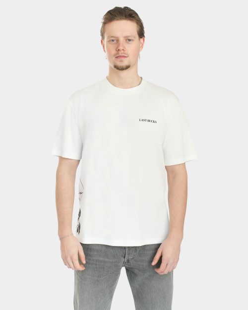 Male model wearing The Balance Side Tee in white, front view, with a small “LAST BUCKS” chest logo and a clean oversized fit