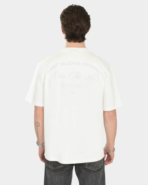 Male model wearing the Own The Sky Tee in White, back view, showing a large tonal back print with “Last Bucks Official” and “Own The Sky”
