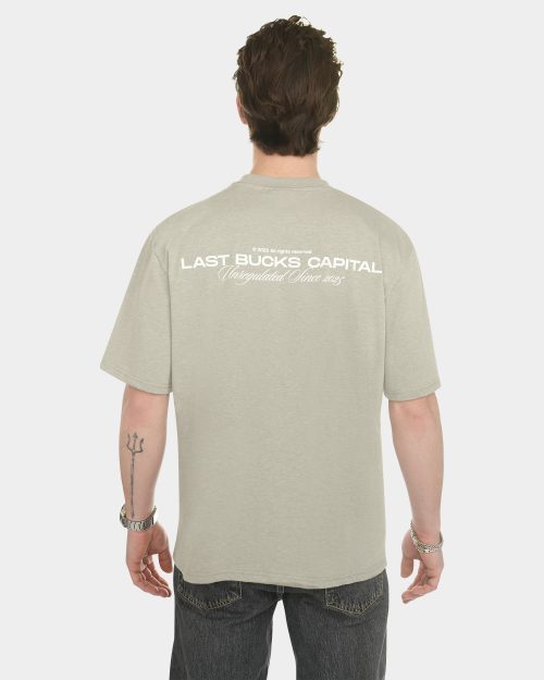 Male model wearing The Capital Tee in Mari Grey, back view, featuring a large “LAST BUCKS CAPITAL” print