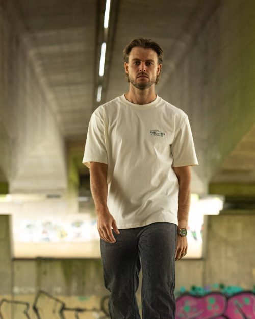 The Iconic Tee Off-White by Last Bucks worn from the front, with the small car and the Last Bucks name on the chest